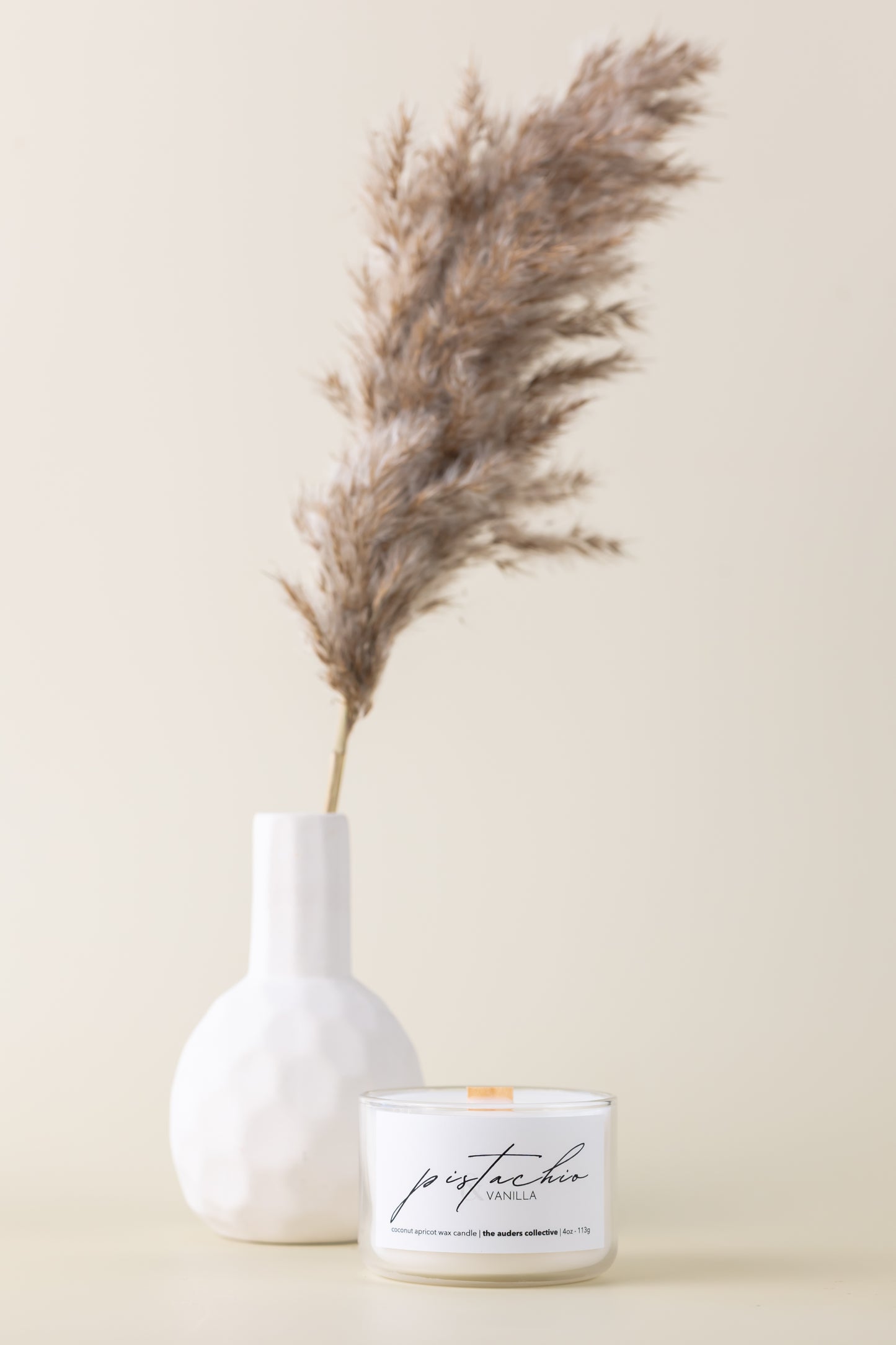 Luxury pistachio and vanilla candle in clear glass jar with decor flower and white vase, perfect for relaxation and minimalist décor