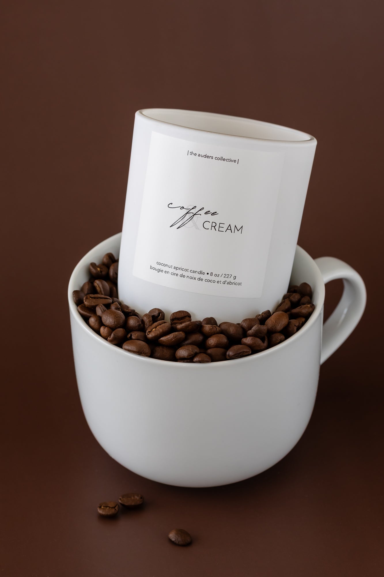 coffee and cream scented candle in a white coffee mug with coffee beans surrounding it 