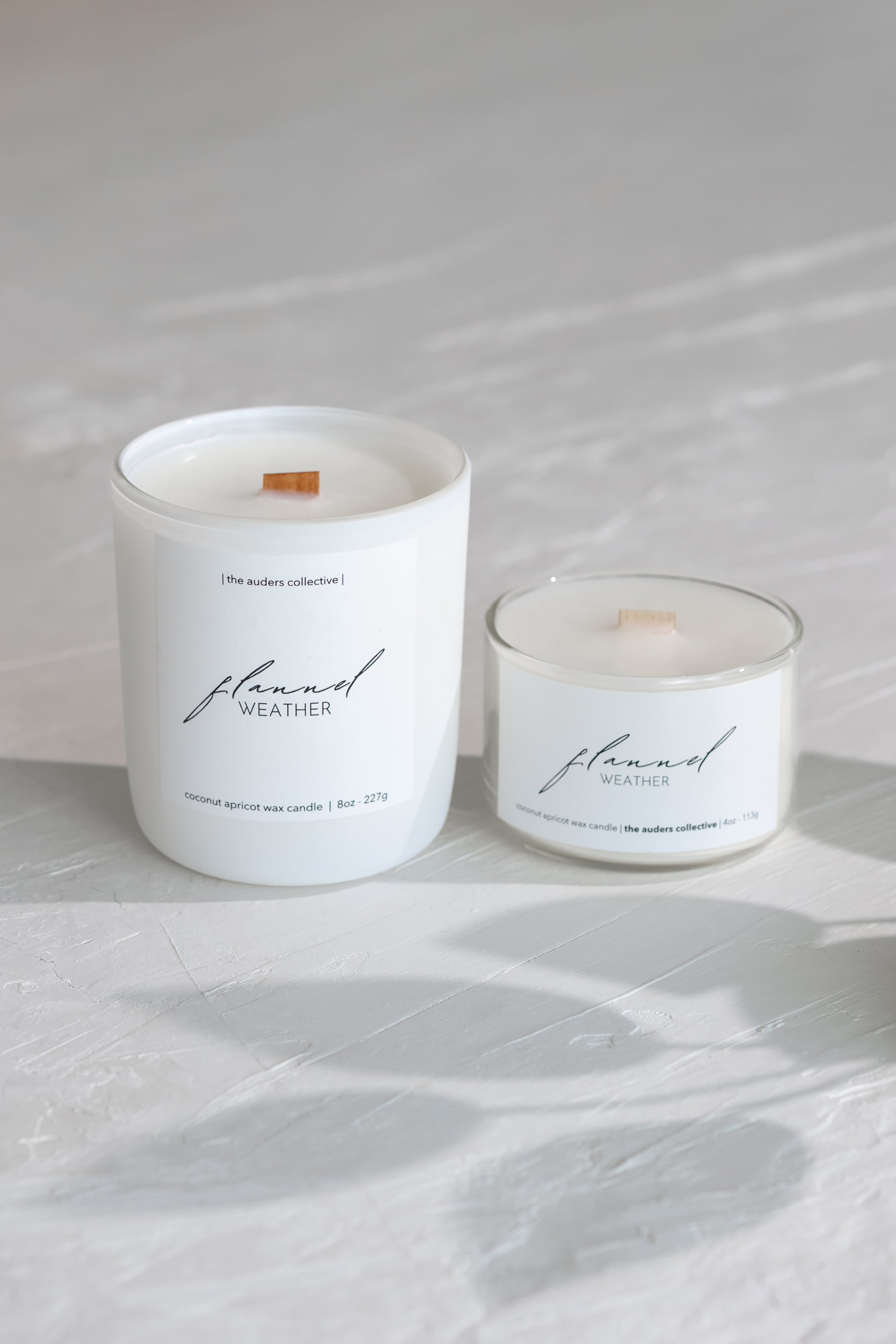 Two white candles labeled 'flannel weather' on a light gray surface.