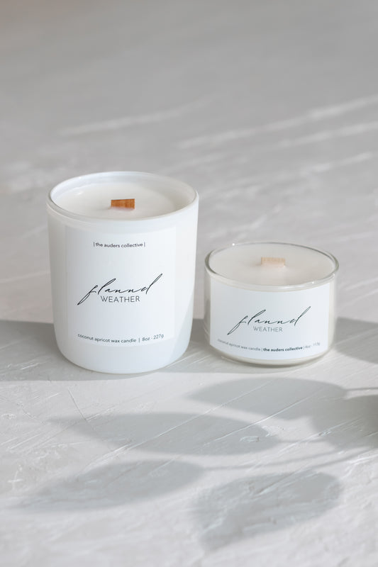 Two white candles labeled 'flannel weather' on a light gray surface.
