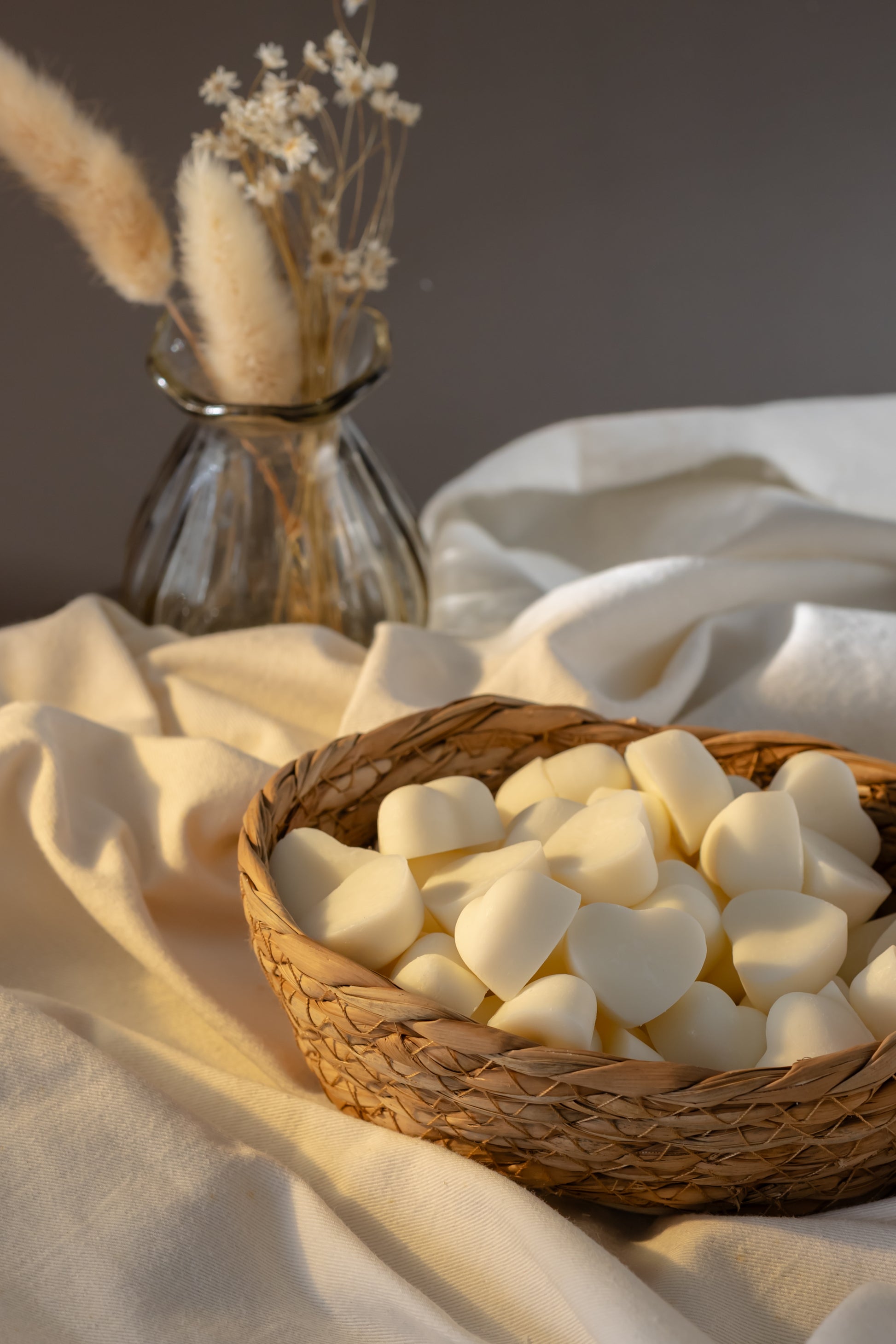 Wicker basket of heart shaped soy wax melts with sun light shining in, white linen draped underneath 