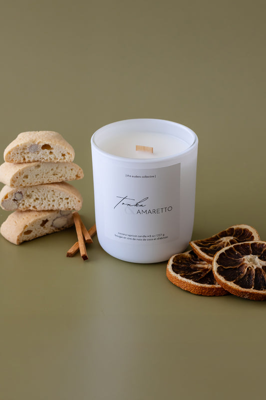 A Tonka & Amaretto scented candle with an almond biscotti and orange slice beside