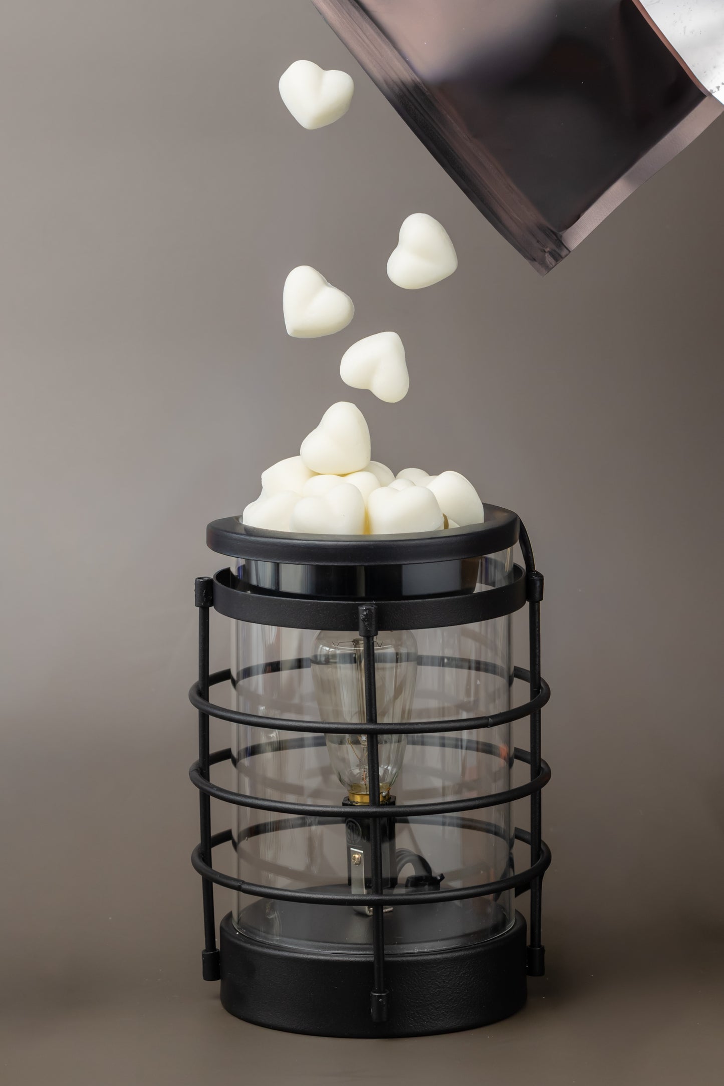 Black wax melter with heart shaped pure soy wax melts being dropped into it from minimalist black bag 