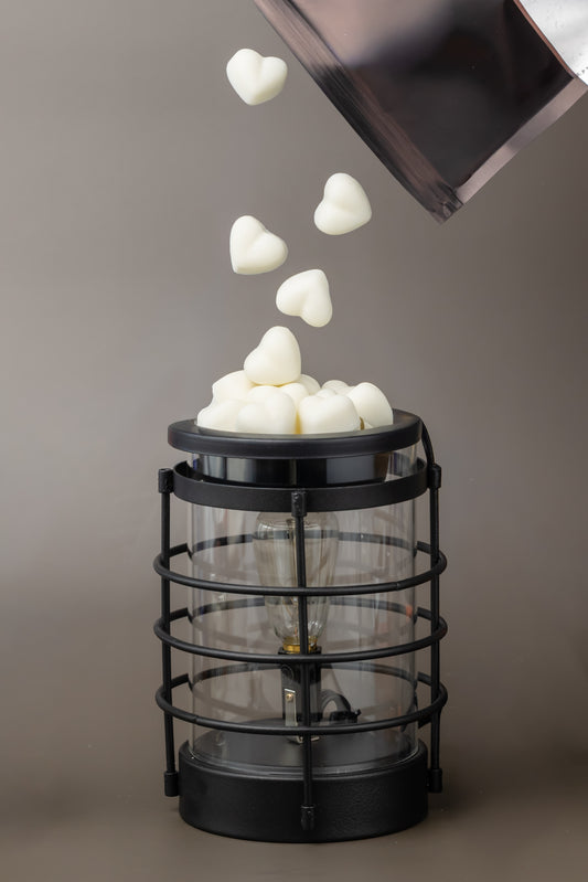 Black wax melter with heart shaped pure soy wax melts being dropped into it from minimalist black bag 